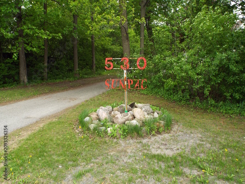 Obraz na płótnie A red metal sign displaying 530 SUNPAC stands proudly above a small roche garden near a pathway, creating a joli site