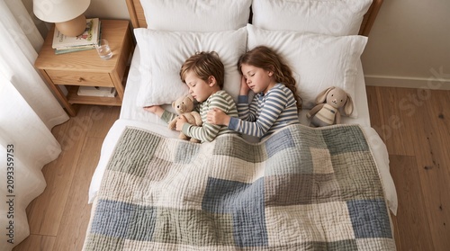 Two young children sleeping peacefully together in a cozy white bed while hugging their soft plush stuffed animal toy friends