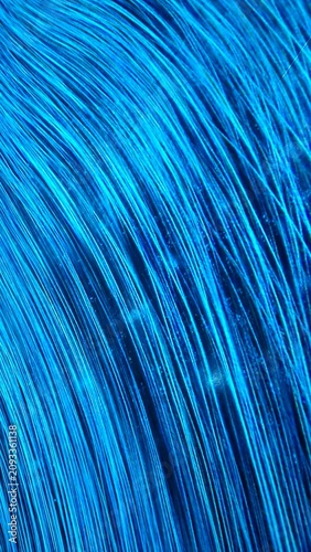 Vibrant blue light trails or synthetic hair strands shimmering in the dark, high tech digital backdrop, vertical.