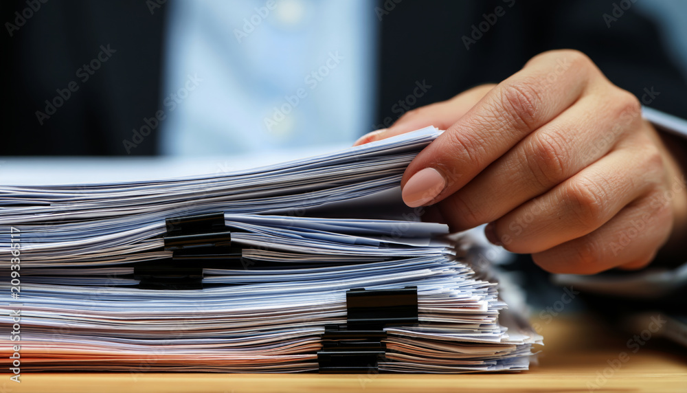 Fototapeta premium close-up of a businesswoman's hand flipping through a thick stack of organized documents