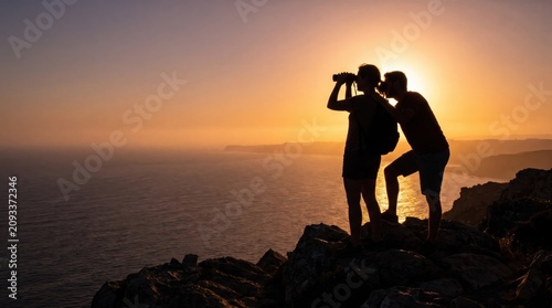 Two silhouetted men observing the ocean with binoculars from a cliff at sunset, exploring and adventuring in nature.