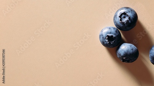 A minimalist flat lay featuring a few blueberries placed in one corner of a pastel beige background with expansive negative space
