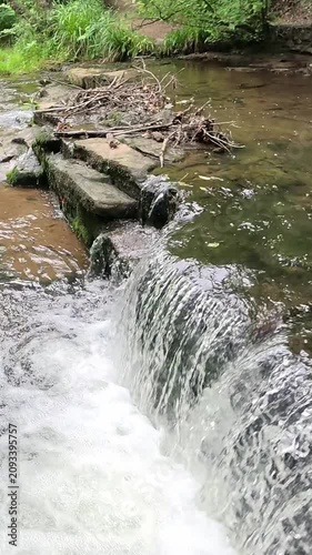 Water cascades over a small woodland waterfall into a gentle stream. Captured in a super slow-motion static shot, every ripple and droplet is revealed amid the tranquil forest surroundings.