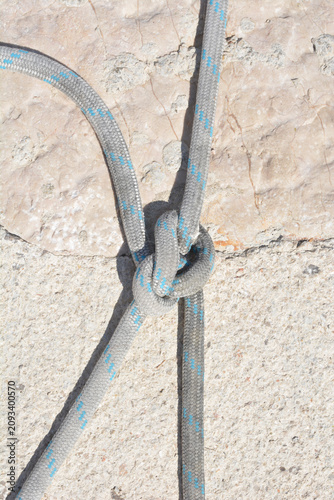 Quadro su tela A grey marine rope with blue accents is tied into a secure bowline on a bight knot against a rough light stone quay at a marina