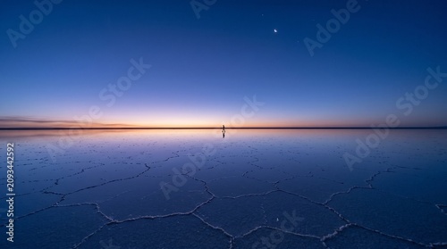salt flat landscape sunset water person distance cracked salt surface blue orange sky peaceful scenery natural wonder evening atmosphere reflection water serene environment