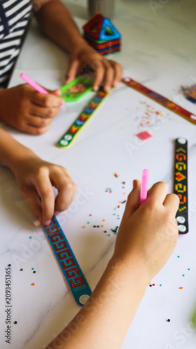 sister and brother are making crafts from diamond mosaics in the form of bracelets on a table in the room close-up