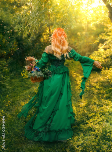 Happy fantasy woman healer. herbalist hand holding basket with herbs for tea flowers essential oil, elf redhead girl walking in sun rays magic light forest green grass trees. fairy dress back view