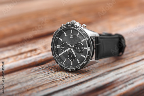 Obraz na plátně A modern silver chronograph wristwatch with a black dial and black leather strap lies on a rustic wooden surface