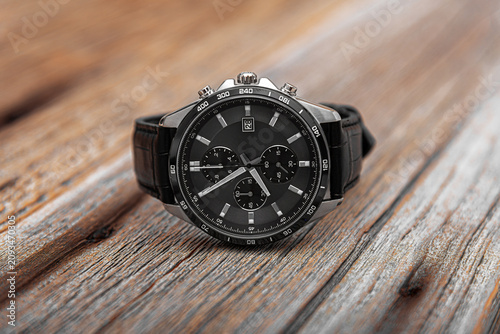 Obraz na plátně A modern men's chronograph watch with a black dial and leather strap rests on a rustic wooden surface