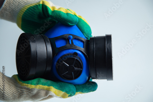 Close-up of hands in construction gloves holding a protective blue mask with two filters on a white background. Concept of personal protective equipment, respiratory protection, repair and