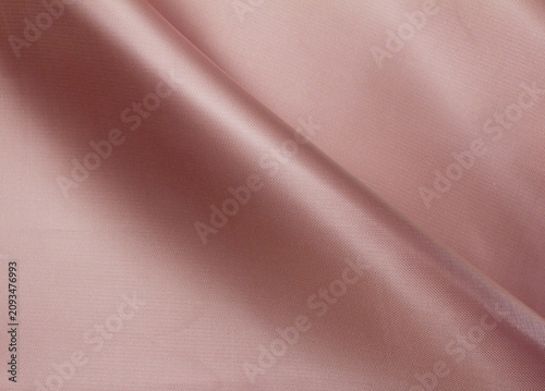 Texture of glossy pink satin polyester cloth. Close up of crumpled pink fabric background.
