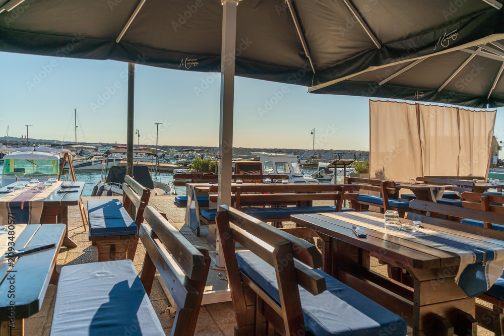 Fototapeta premium Outdoor restaurant terrace overlooking marina with boats on sunny summer day