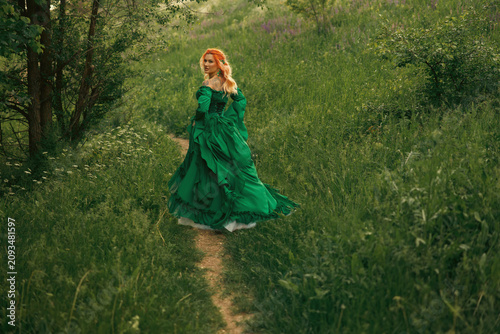 Happy fantasy woman medieval queen noble lady walking in summer nature footpath. elf redhead girl princess running at forest path green grass trees. fairy tale noble lady in long dress looking back