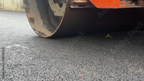 Road Roller Compacting Asphalt: A close-up view of a road roller's drum pressing down on a freshly paved asphalt surface, smoothing and compacting the material for a durable road.