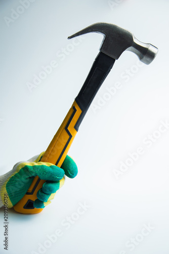 Close-up of a gloved hand holding a raised hammer with a metal head on a white background in the center. The concept of repair, construction, tools, hammering. High quality photo