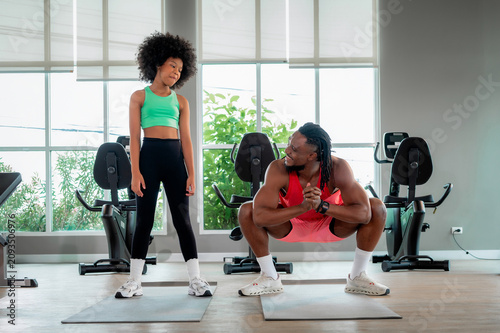 Black fitness coach dad showing squat exercise afro hair girl. Scene for family wellness, personal trainer mentoring child, bodyweight workout and health communication.