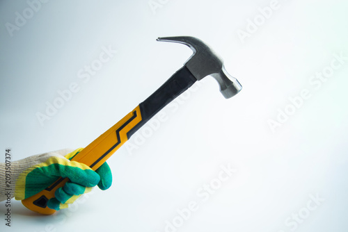 Close-up of a gloved hand holding a raised hammer with a metal head on a white background with space for text. The concept of repair, construction, tools, hammering. High quality photo