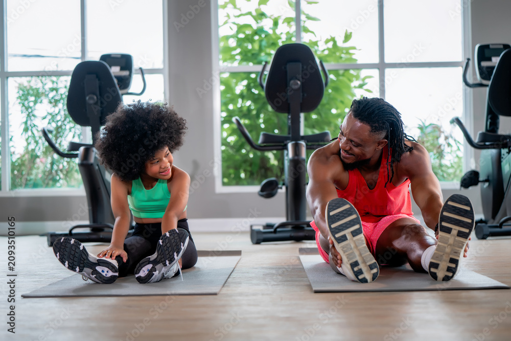 Fototapeta premium African American father daughter stretching legs yoga mat gym. Concept of family fitness, healthy active lifestyle, flexibility training and strong family bonding.