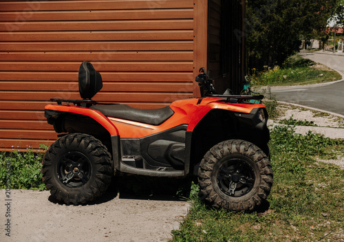Orange all-terrain vehicle parked beside a wooden building in Montenegro. Off-road transport commonly used in mountain and rural areas.