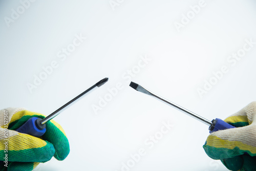 Close-up of two hands in work gloves holding screwdrivers against a white background. Concept of repair, handyman, tools, construction, installation. High quality photo