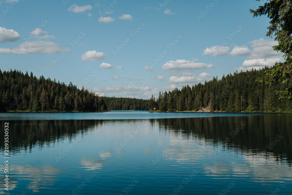 Fototapeta premium Evergreen forest reflected across the still waters of Black Lake in Durmitor National Park, Zabljak, Montenegro. Beautiful mountain landscape beneath scattered summer clouds.