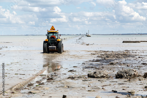 Tracteur, tractopelle, nettoyant une route inondable et submergée par la mer, à marée descendante pour enlever la vase. Le Gois à Noiurmoutier.