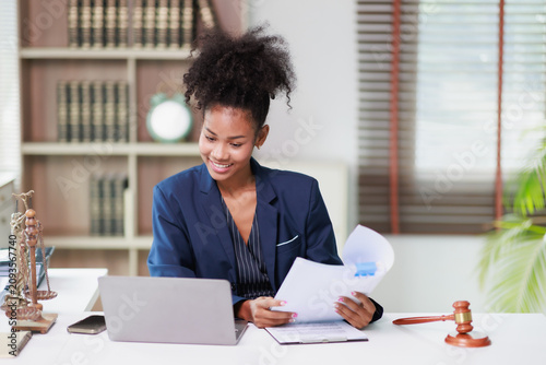 African American female legal professional working in an office, reviewing documents and using a laptop, embodying concepts of law, justice, and professional empowerment
