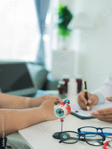 An ophthalmologist is explaining eye treatment to a patient holding a pair of damaged glasses, while an optometrist is consulting with a male patient.