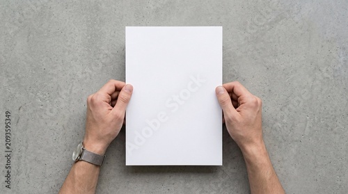 Flat lay of a person holding an empty white letterhead paper mockup on a minimalist gray desk surface.