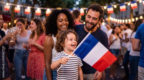 A laughing toddler waves a French flag in front of joyful parents at a crowded Bastille Day street party for candid family stock photography