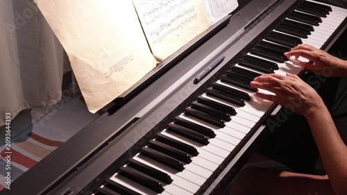 Close-up of piano keys in dark tones as woman plays gentle classical music on digital piano, student practicing piano lessons, horizontal video