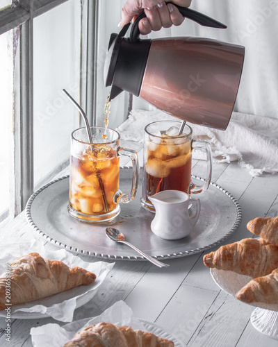 Glasses of iced coffee with a hand pouring coffee into one from a carafe.