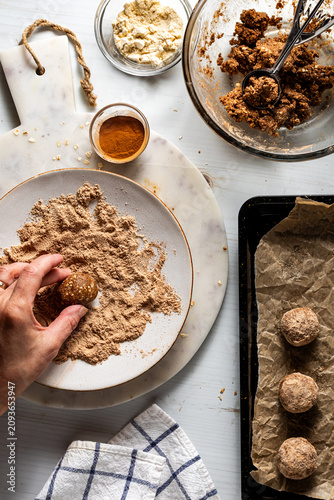 A hand coating an energy ball in a mixture of cinnamon and protein powder.