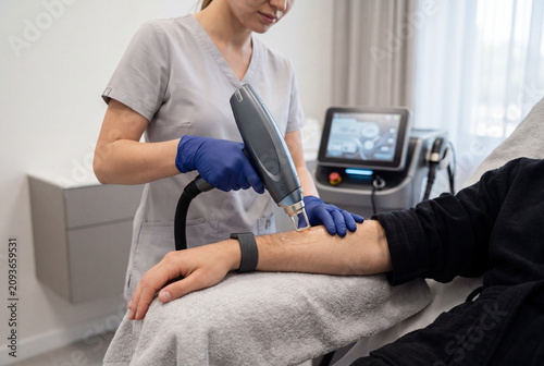 Aesthetician performing laser hair removal on man's forearm