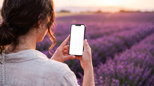 Hand holding mobile phone with blank white screen in lavender field during sunset, woman using smartphone for nature photography app mockup, summer vacation lifestyle, floral travel.
