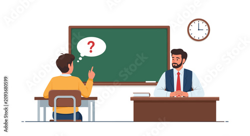 Schoolboy raising hand to ask question to male teacher sitting at his desk in classroom with green blackboard.