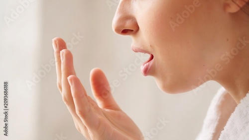 A close up profile photograph of a woman exhaling air from her open mouth and hand female person human face side