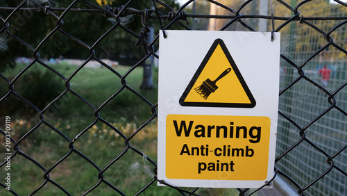 фотографія Anti-climb paint warning sign, security fence, yellow caution notice on chain li
