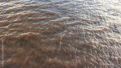 Brown river water surface featuring natural ripples and sediment-rich texture. Ideal as an abstract background for environmental, hydrology, freshwater, and nature concepts.