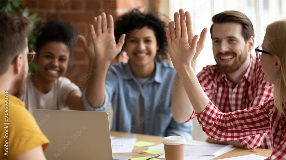 Fototapeta premium Diverse group of smiling colleagues giving high fives in a modern office meeting celebrating teamwork and success