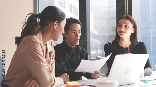 Three business professionals discussing charts and reports while analyzing information on laptop during collaborative office meeting.
