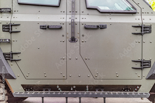 Close-up view of military armored vehicle side panel, featuring robust industrial design with rivets, hinges, and modular compartments, textured metal step for access, olive green paint against