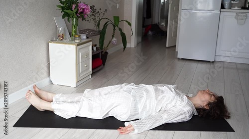 Static Shot Of Woman Moving From Seated Pose To Full Recline On Yoga Mat During Gentle Relaxation Exercise In Bright Home Living Room.