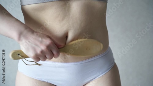 Static Shot Of Woman Brushing Abdomen With Wooden Massage Brush During Body Care Treatment In Neutral Studio Background For Skin And Wellness Routine.