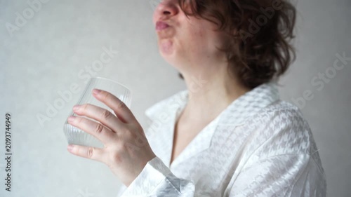 Static Shot Of Woman Drinking Water From Clear Glass In White Shirt Against Plain Indoor Background.