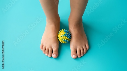 Childs feet standing next to a yellow and blue spiky massage ball on a turquoise background