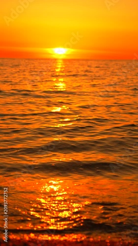 Sunset ocean beach scene featuring golden waves washing onto the pebble shore under a brilliant orange evening sky for a peaceful mood