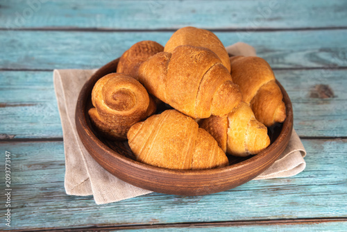 Freshly baked puff pastry croissants in a traditional clay bowl. Morning dessert with coffee or tea.