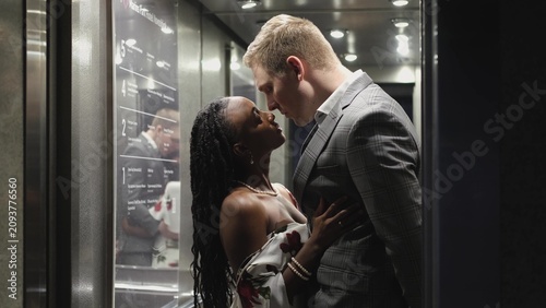 Schilderij op canvas A handsome young man and a beautiful woman look at each other and smile while standing in an elevator