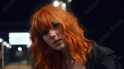Portrait of a beautiful fiery red-haired woman on a city street at night.